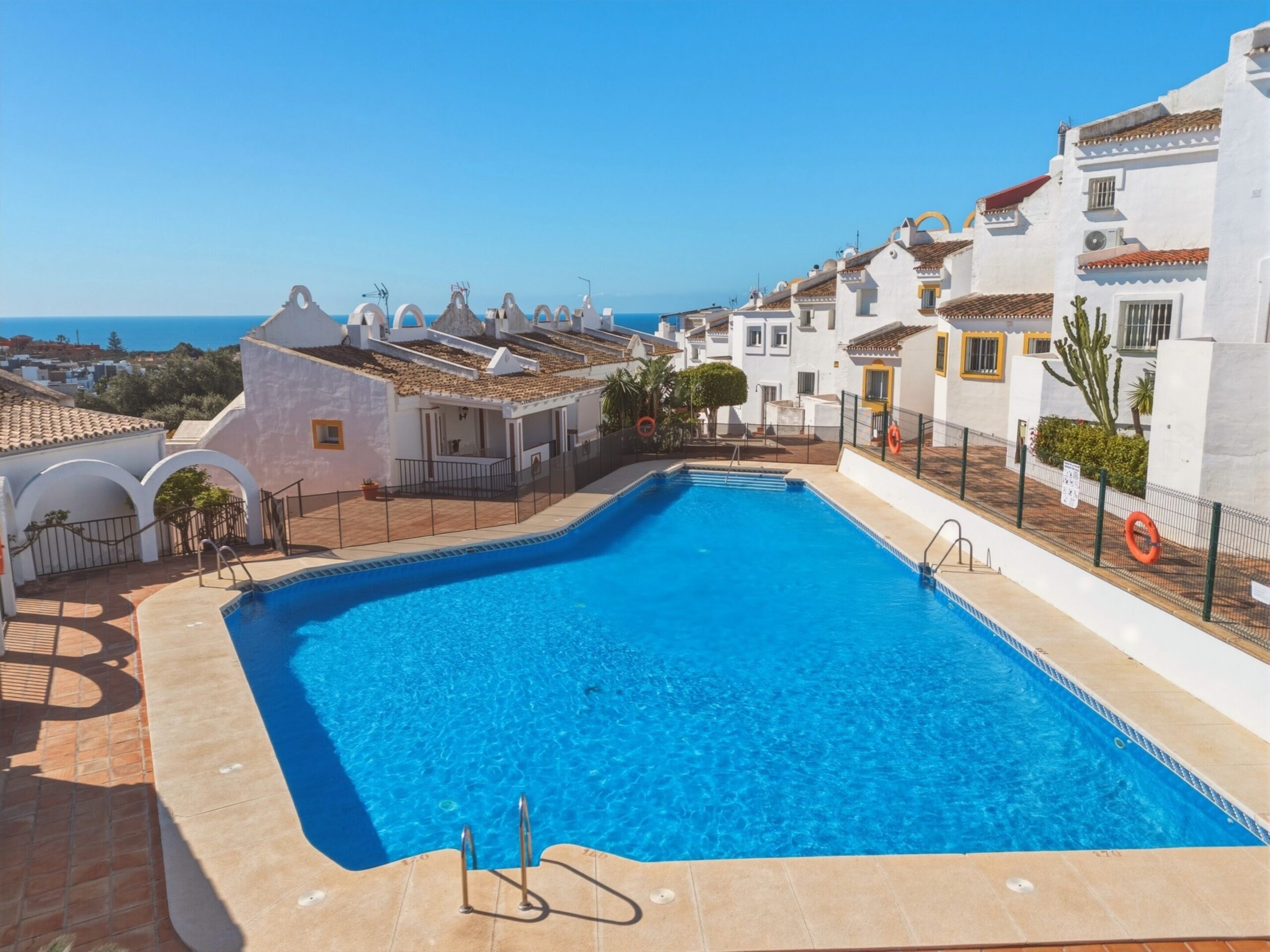 The communal outdoor pool of the residence, with white Mediterranean houses and the sea beyond