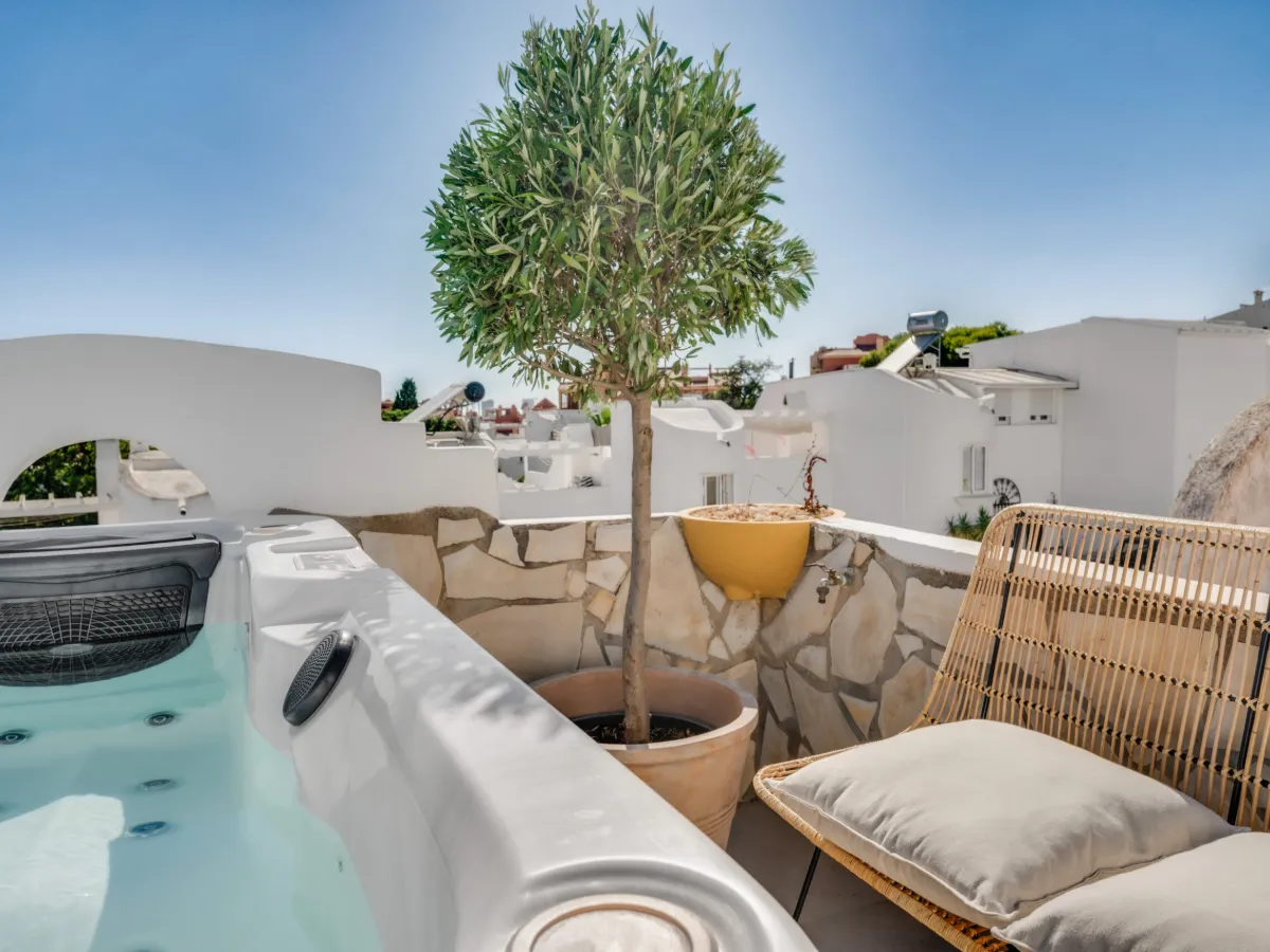 Private roof terrace at Casa Cabopino Retreat with the heated jacuzzi, an olive tree and a rattan lounge chair under a blue sky