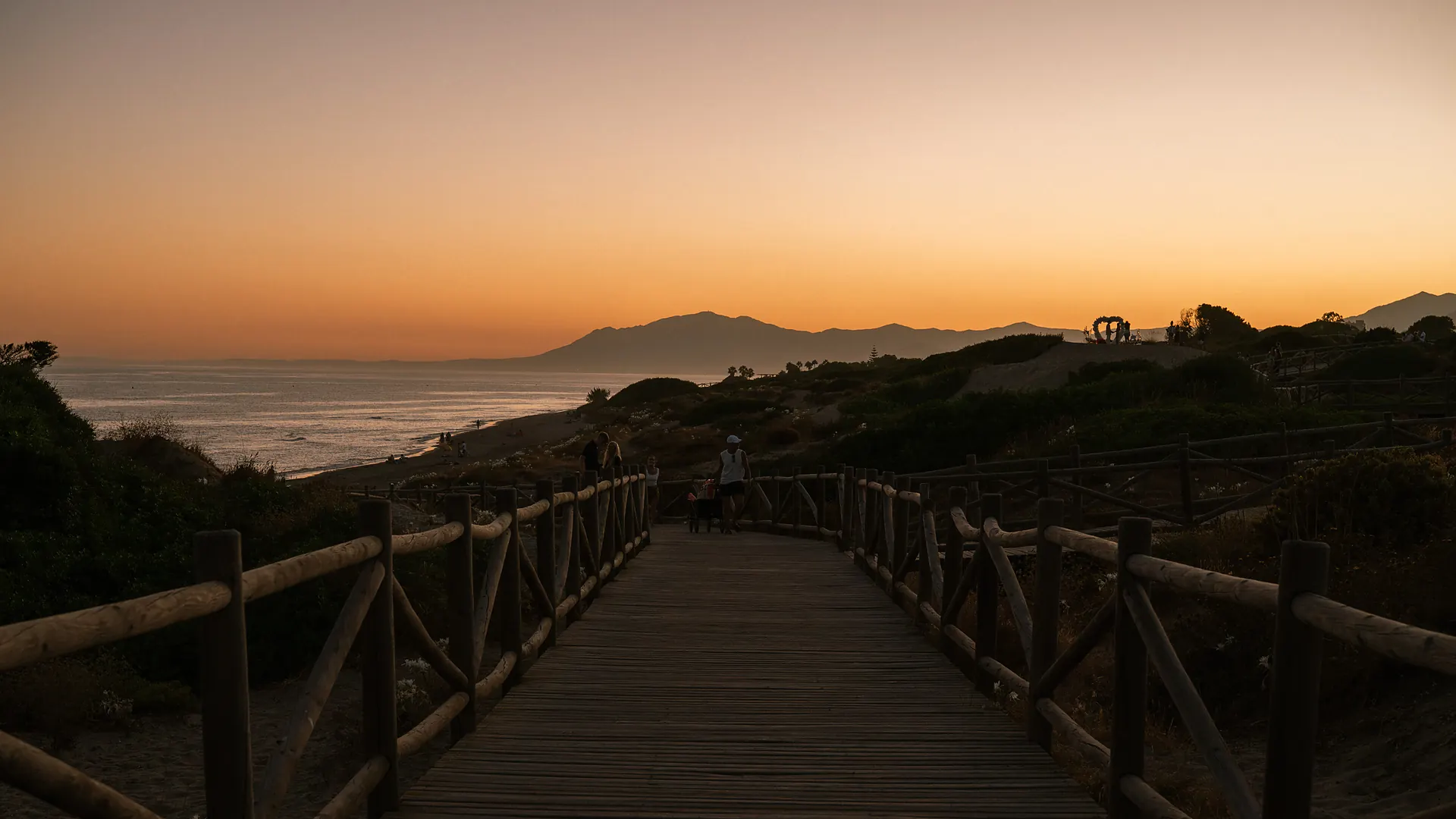 Wooden boardwalk through the Artola Dunes towards the sea at sunset