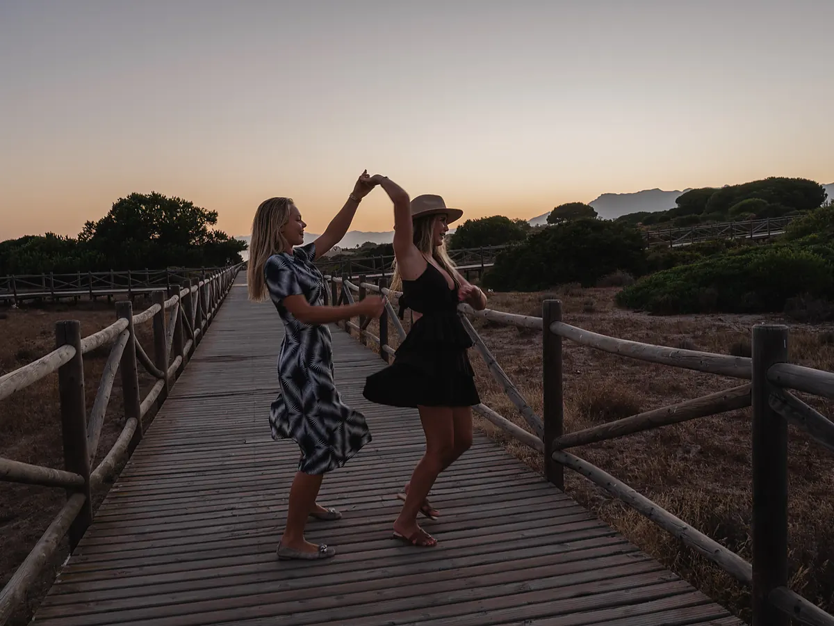 Two guests dancing on the wooden boardwalk through the dunes at golden hour