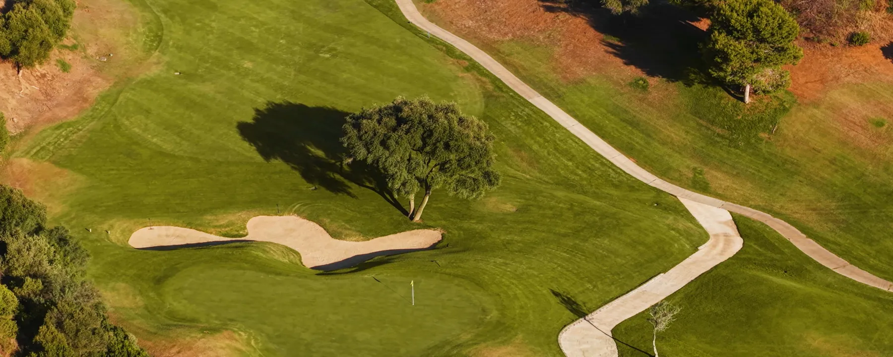 Aerial view of a golf green, bunker and pathway between pines in the hills of Marbella East