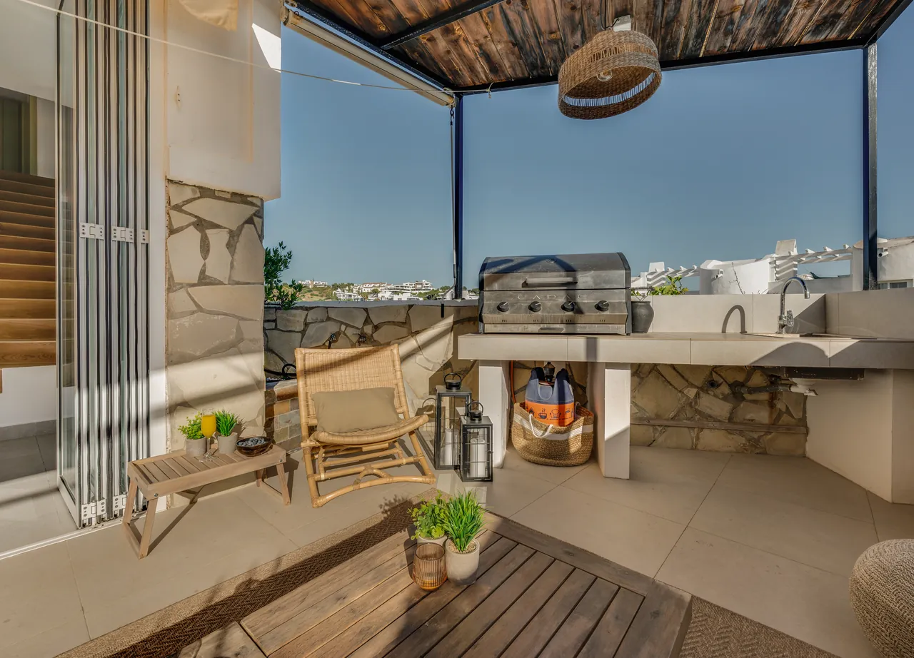 Outdoor kitchen with barbecue and sink on the covered terrace, with white rooftops and the sea beyond
